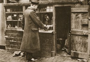 Un zapatero, establecido en un puesto improvisado en un callejón adoquinado de Mayfair, recibe botas de un chófer, de Maravilloso Londres, publicado 1926-27 de English Photographer